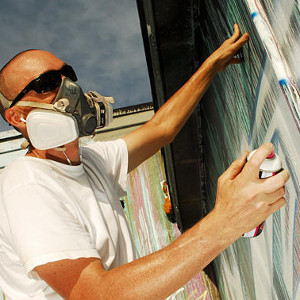 Photo of Artist, Bellichi, in the process of spray painting a mural.